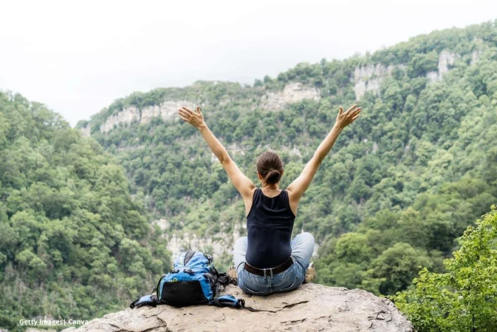 Mujer con los brazos abiertos en la cima de una montaña, rodeada de naturaleza, en un momento de digital detox al aire libre.