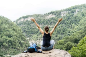 Mujer con los brazos abiertos en la cima de una montaña, rodeada de naturaleza, en un momento de digital detox al aire libre.