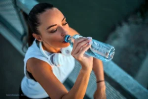 Mujer bebiendo agua de una botella plástica después de hacer ejercicio, ejemplo de hidratación consciente.